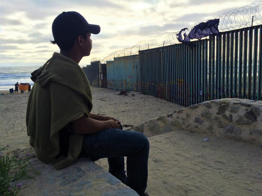 A boy sits on a beach in Tijuana, Mexico and looks at the US border wall