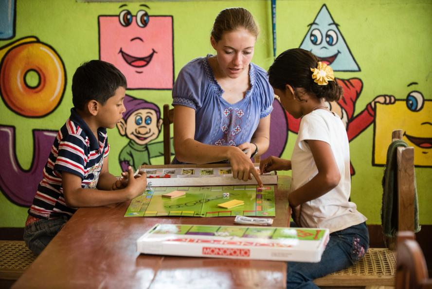 a woman and two children sitting at a table playing Monopoly board game