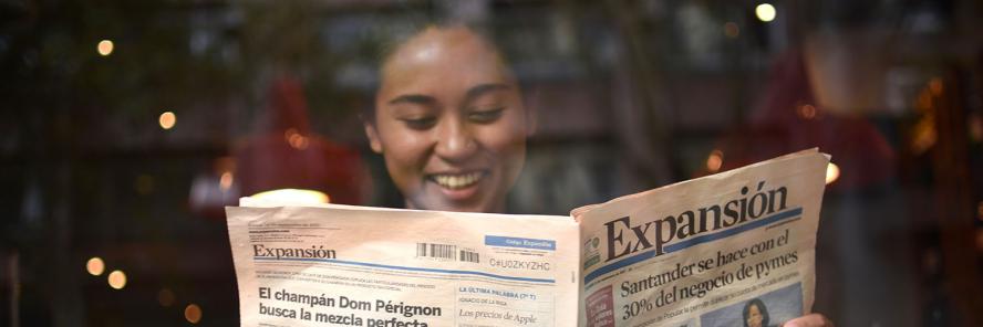 Young person in a coffee shop reading a Spanish newspaper