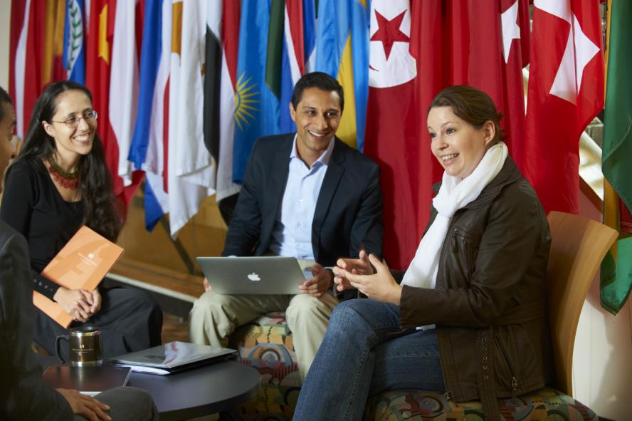 three people sitting and smiling in front of a row of flags on flagposts