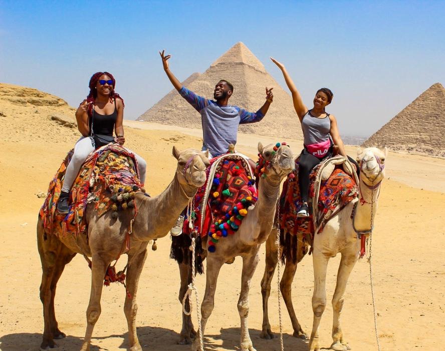 Three Tufts students ride on camels in front of pyramids in Egypt