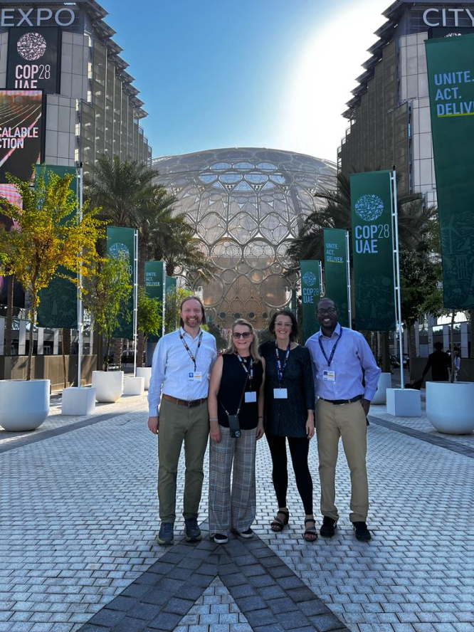Fletcher faculty, staff, and students stand in front of the entrance, which is a large glass dome, to the COP UN Climate Change Conference in the UAE