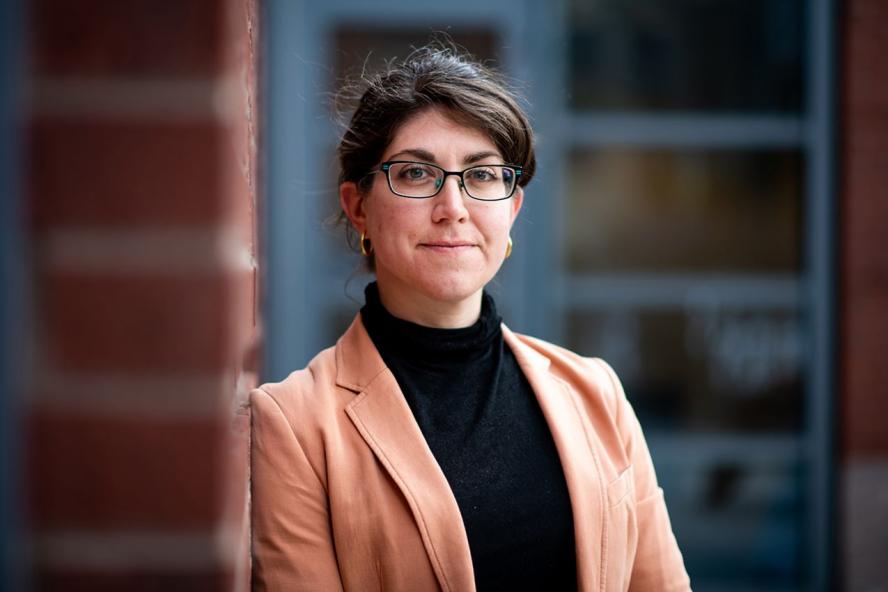Woman in orange blazer leaning on brick wall of building