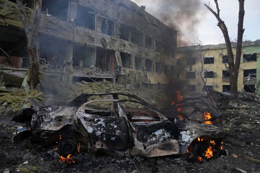 A car burns in front of a hospital building damaged by shelling during Russia’s invasion of Ukraine.