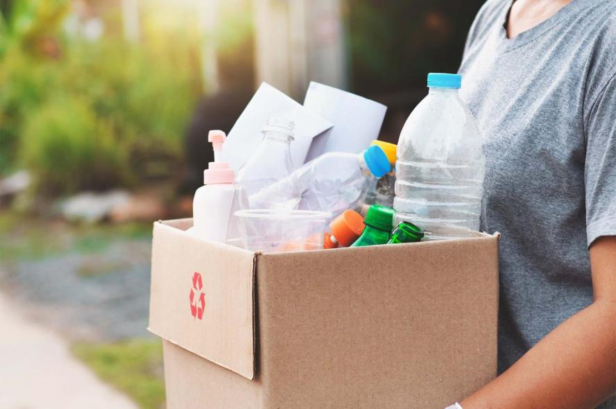 A person carries a box filled with recyclable items.