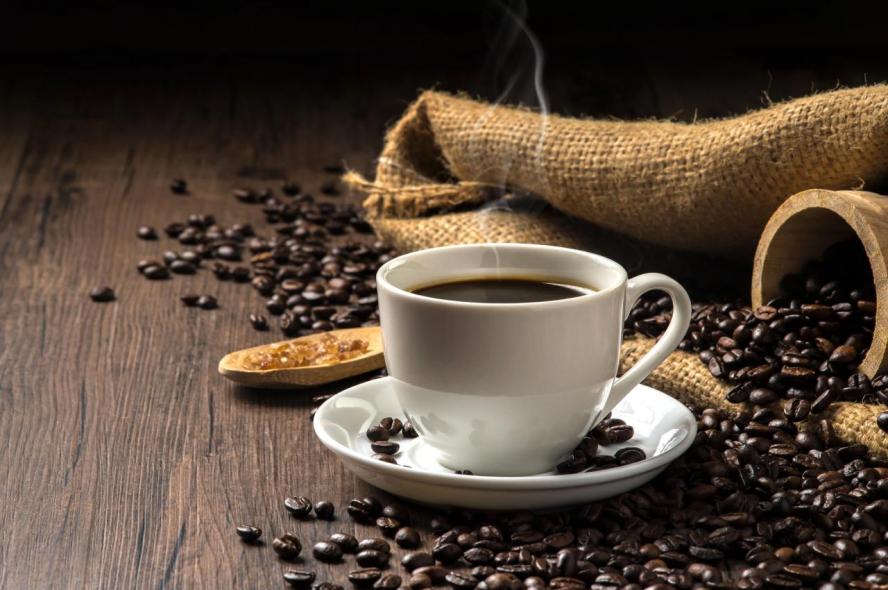 A steaming cup of coffee with coffee beans and burlap bag. A scientist explains how caffeine gives people what feels like a boost of energy.