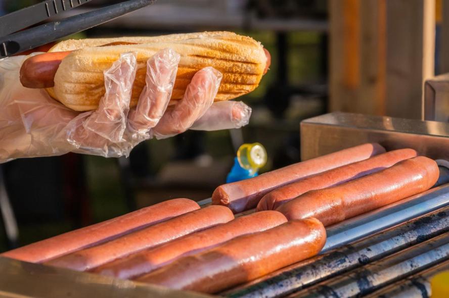 Hot dogs roasting on a grill with one being put in a bun