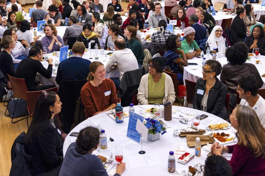 Event attendees seated at round tables eat and and talk animatedly 