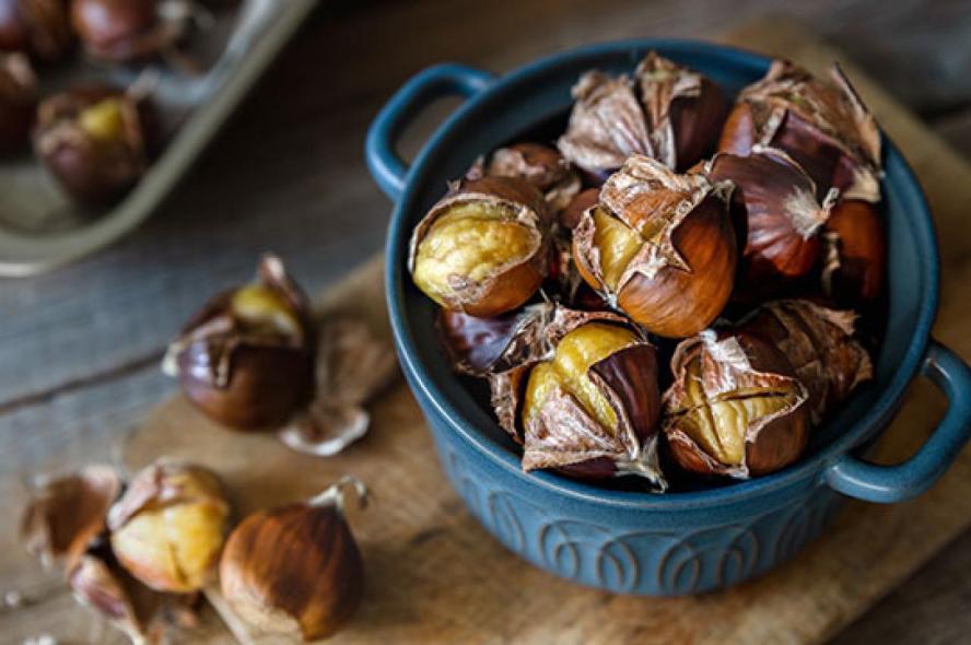 Oven roasted sweet chestnuts with open shells close up top view on wooden board