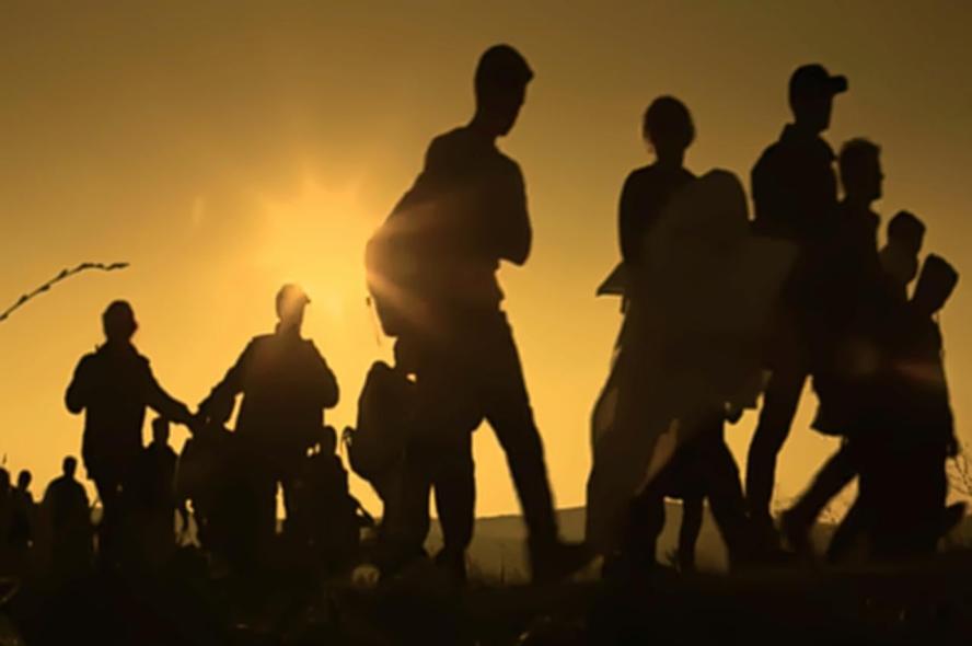 Migrants walking along a track, seen in profile only.