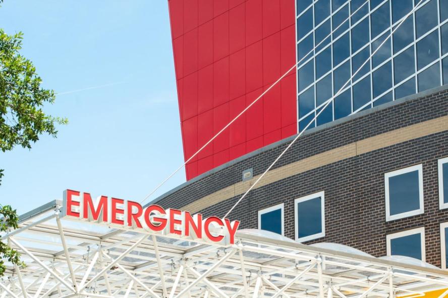 The outside of a hospital with the sign “emergency” above an awning.