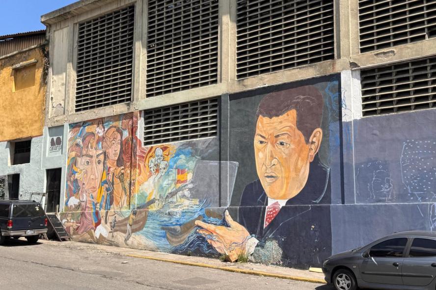 An empty street in Caracas, Venezuela, with a large mural of Hugo Chavez and a variety of other faces, and a collection of skulls. 