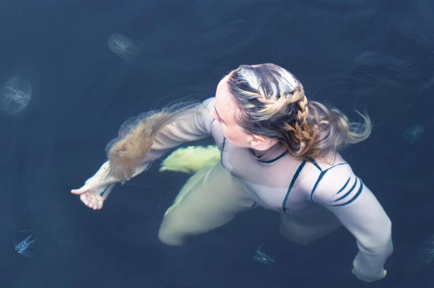 A woman in costume interacts with sea creatures in the ocean