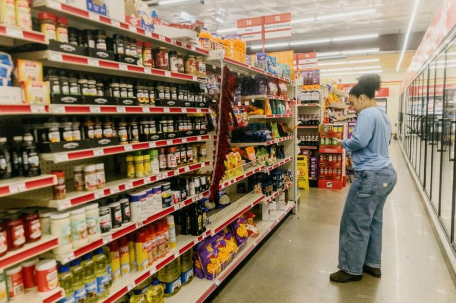 A woman looks at a nutrition label while standing in a grocery aisle full of different food items
