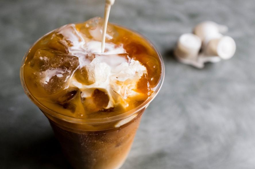 A cup of iced coffee with cream being poured into it