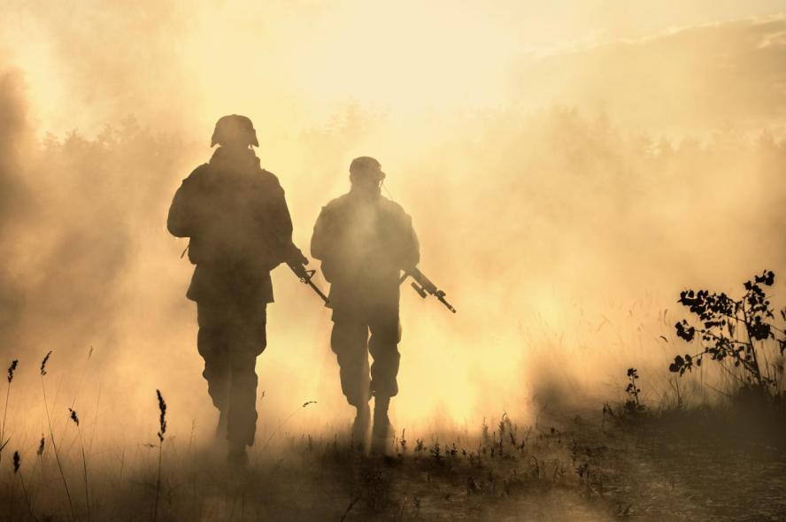 Two soldiers carrying guns walk through a smoky landscape