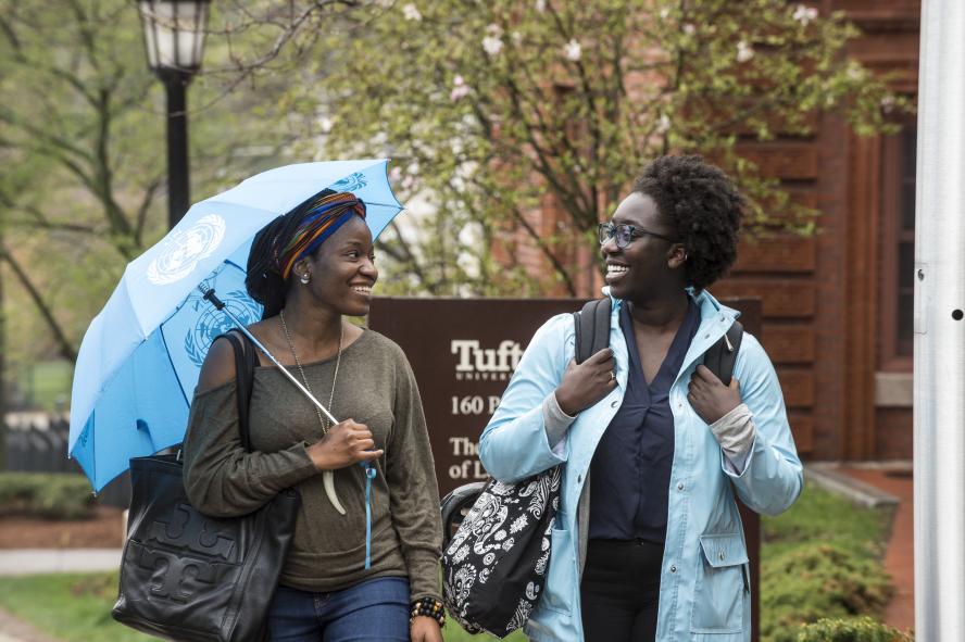 two students walking and talking on Tufts' campus on a rainy day