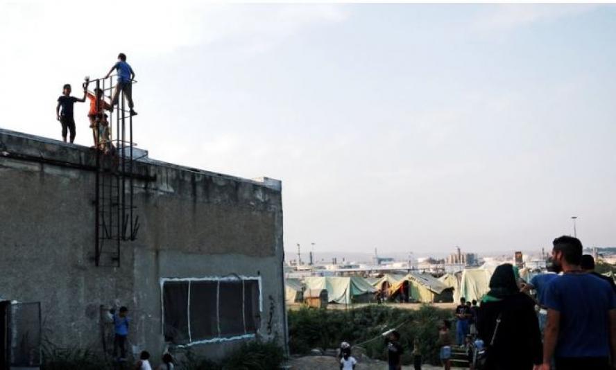 People climb a metal ladder up the side of a building, while others look over a tent city