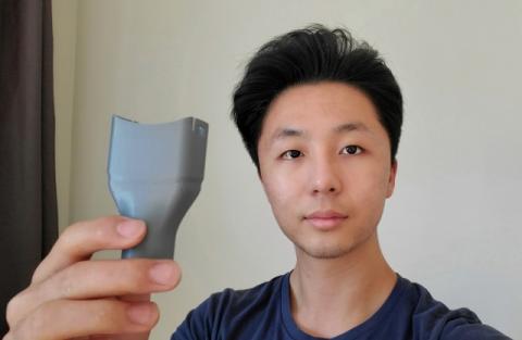 William Liu holds a gray adapter he printed at the Nolop Fabrication, Analysis, Simulation, and Testing facility at Tufts. 