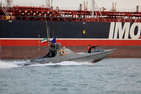 A speedboat racing in water with machine gun and Iranian flag  near a large oil tanker. Confrontations between the U.S. and Iran have far more to do with domestic U.S. politics than they do with any intention to go to war, says a Tufts expert