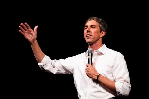 Beto O’Rourke standing on a stage with a microphone. We need smart, strategic, and compassionate leadership in our nation, O’Rourke tells a Tufts podcast.