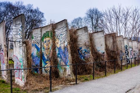 Large pieces of concrete wall with graffiti on them, on display behind a railing. The fall of the Berlin Wall thirty years ago unified Germany and reshaped the map of Europe 