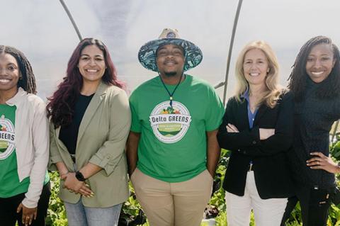 five individuals posing for a group photo in a greenhouse