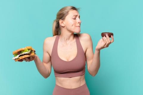 woman in running outfit holds a sandwich and doughnut looking confused