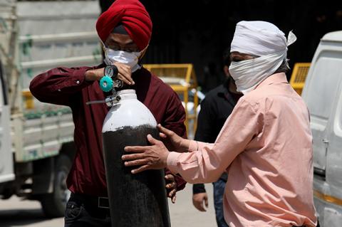 Two men wearing protective masks carry an oxygen tank from a gas supplier in New Delhi.  