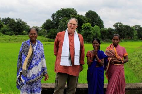 Trickle Up president Bill Abrams stands with three women in a field in India. Abrams has led the international nonprofit Trickle Up for the last 16 years, working to help the poor start businesses, earn, and save.