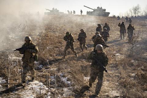 Soldiers with rifles walking on a leafy hill, with tanks in the background. As the Ukraine war enters its second year, Tufts experts weight alternative endings—and the possibility it won’t be resolved any time soon.
