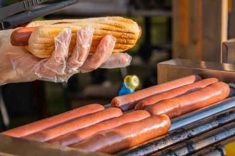 Hot dogs roasting on a grill with one being put in a bun