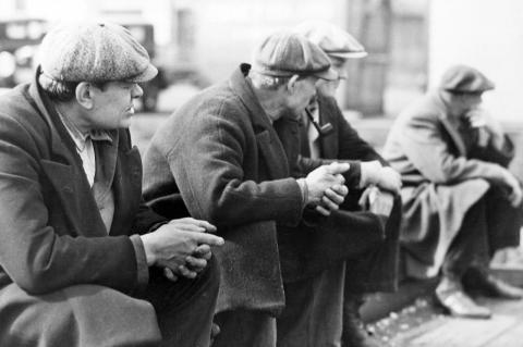 Black and white photo of four men in caps sitting in a row in the 1930s. 