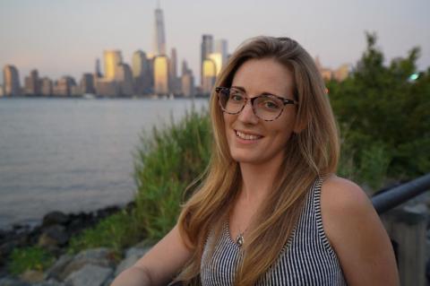 Meg Reilly stands outdoors with water a city skyline behind her