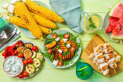 Tips for Safe and Healthy Summer Cookouts A picnic table covered in plates of corn, squash, chicken, watermelon and other healthful foods.