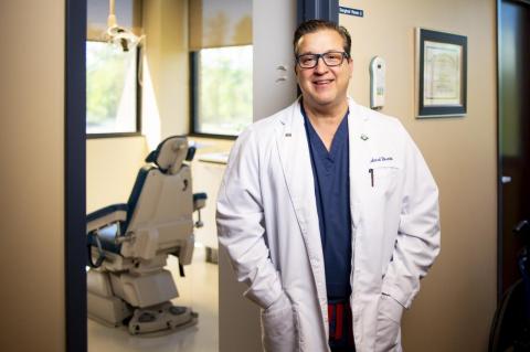 The Next Leader of America’s Dentists Sees Opportunity in This Moment Richard Rosato in blue scrubs and a white dental coat in his office, a dental chair visible in background