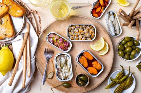 An overhead view of a table set with varieties of tinned fish, toast, and other snacks.