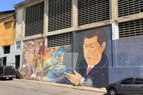 An empty street in Caracas, Venezuela, with a large mural of Hugo Chavez and a variety of other faces, and a collection of skulls. 