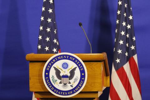 A podium with a U.S. State Department seal on the front and two U.S. flags beside it