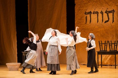 Women dance around on a stage with a sheet