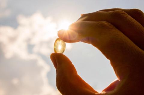 A vitamin D supplement pill is held up in the sunlight, a main source of vitamin D