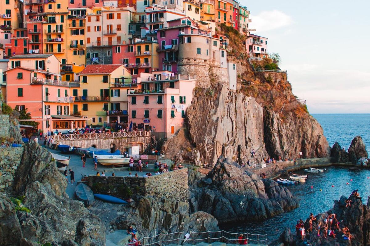 Colorful houses are built into the Italian cliff, overlooking a harbor with boats