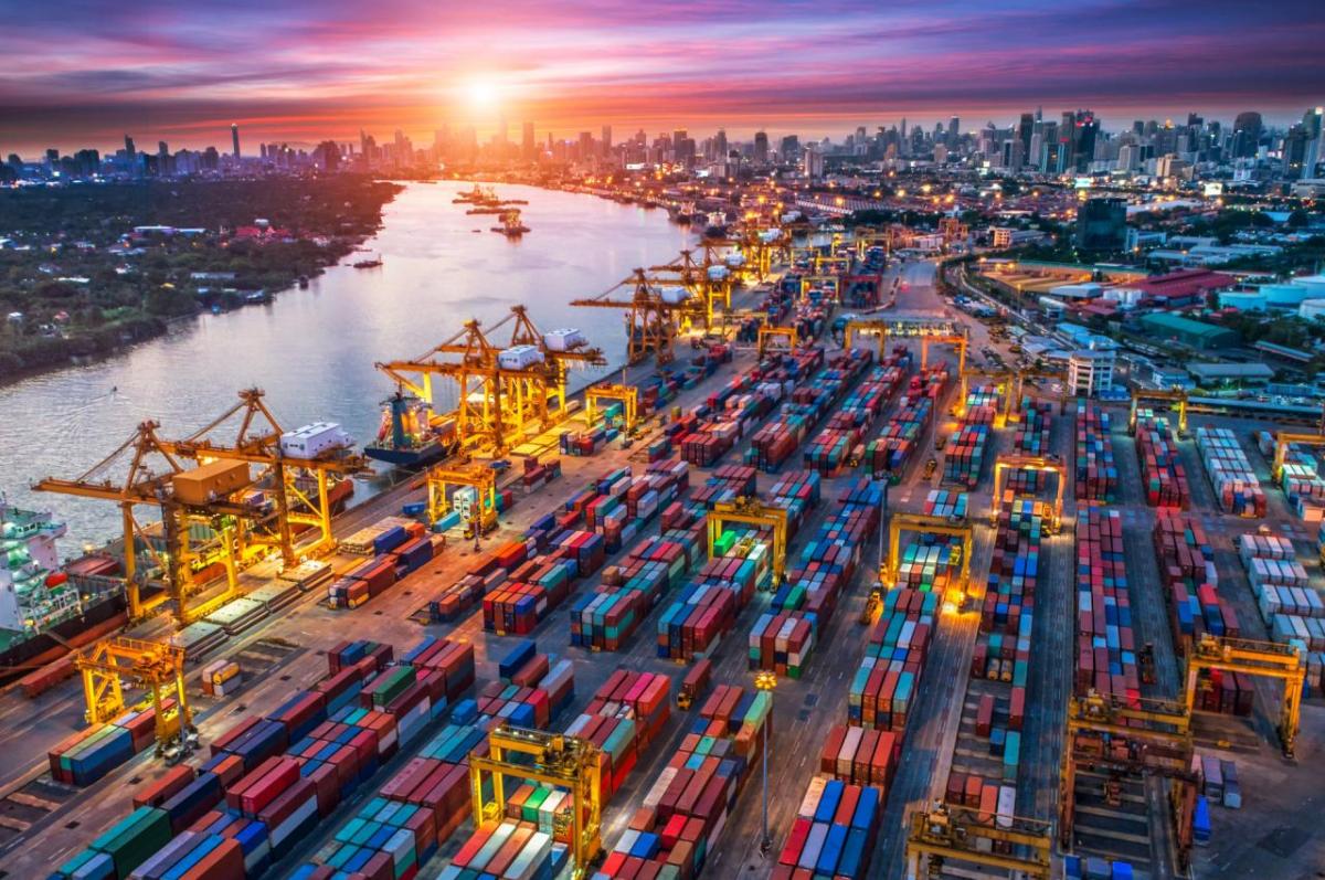 Aerial photo of a shipping yard with many shipping containers and cranes on a river at sunset. 