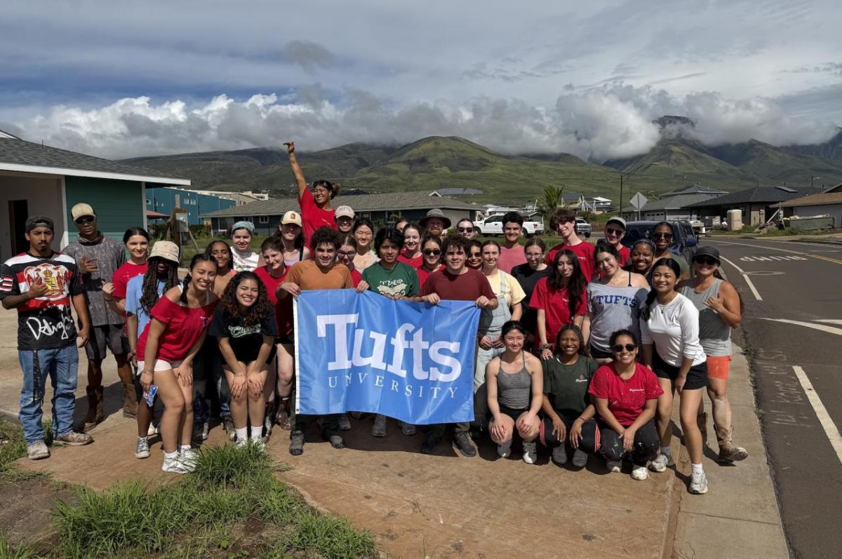 A large group of people stand in front of mountains holding a flag that says Tufts